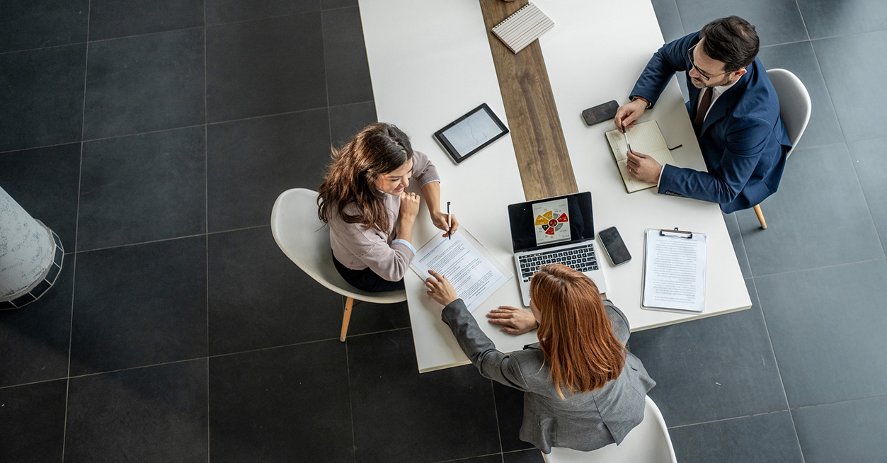 Vista dall’alto di tre persone sedute attorno a un tavolo in ufficio mentre esaminano documenti